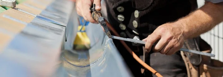 Person lötet Dachrinne